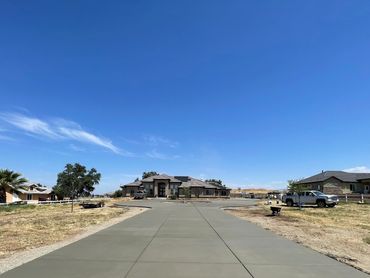 Long concrete driveway leading to a large suburban house under a clear blue sky.