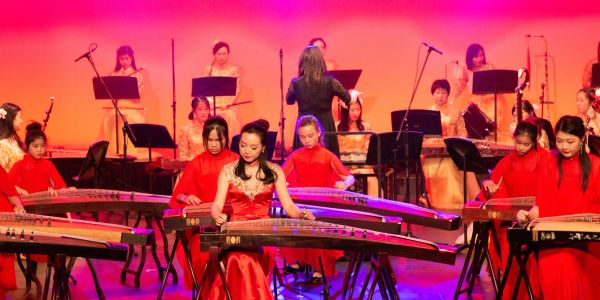 Musicians in red dresses playing guzheng on stage.