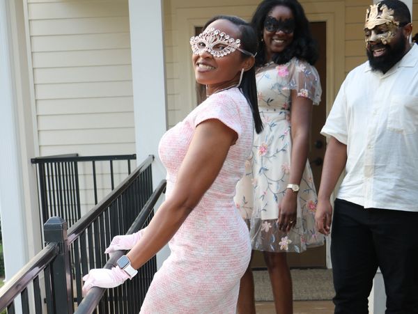 Three people wearing elegant masquerade masks and stylish outfits on a porch.