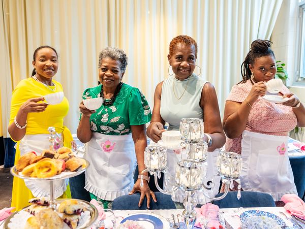 Four women enjoying tea together, wearing aprons and holding teacups.