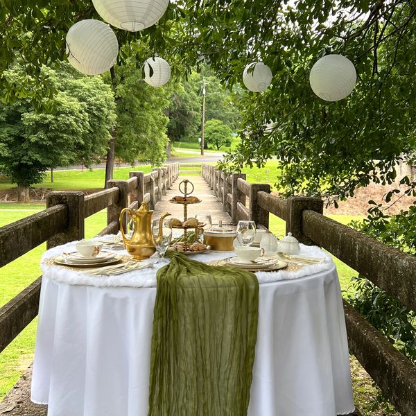 Elegant outdoor tea table setup with white lanterns hanging above on a wooden bridge.