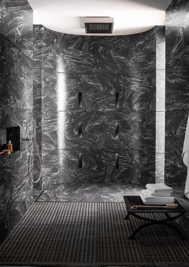 Modern shower with black marble walls, multiple showerheads, and a towel rack.