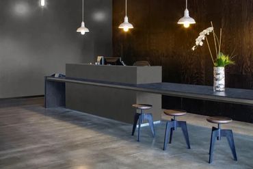 Minimalist reception desk with three stools and hanging lights in a modern space.