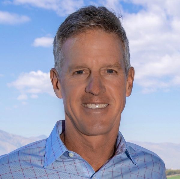 Smiling man in blue checked shirt outdoors.