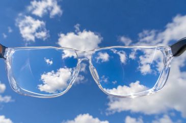 Clear eyeglasses showing a blue sky with white clouds.