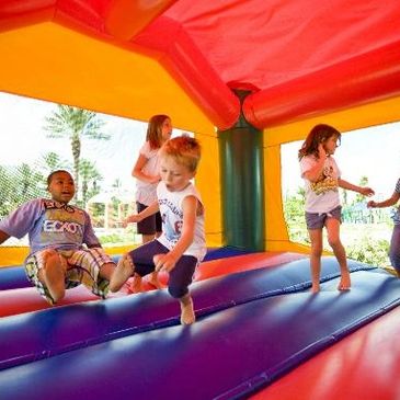 A group of friends jumping around inside a Bounce house during a birthday party.