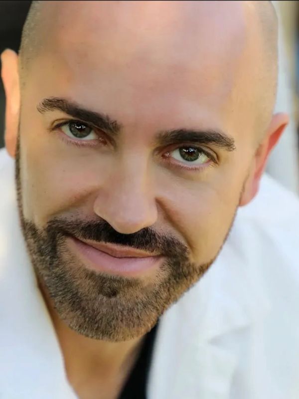 Close-up of a smiling bald man with a beard and green eyes.