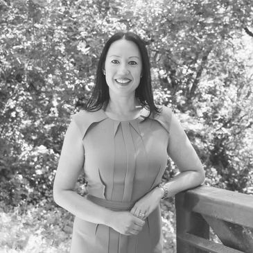 A smiling woman in a dress standing outdoors by a wooden railing.
