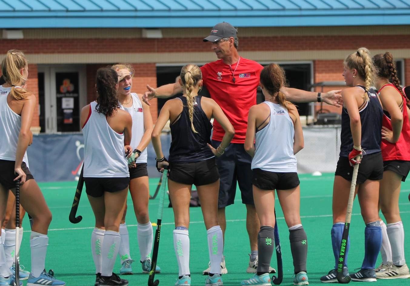 Coach instructing female field hockey players on turf.