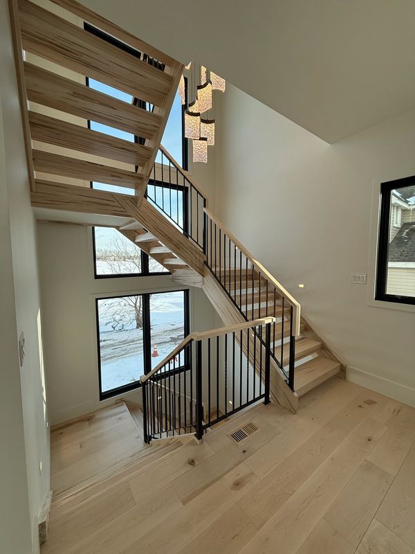 Wooden staircase with black railing and large windows.