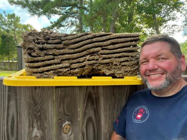Man smiles next to a large stack of honeycomb frames outdoors.