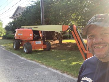 Man smiling next to an orange boom lift on a sunny day.