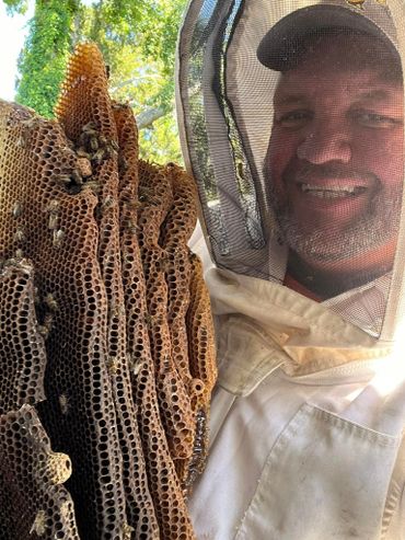 Beekeeper smiling with a large honeycomb full of bees outdoors.
