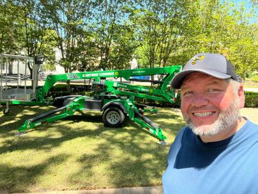Man smiling outdoors with a green Sunbelt Rentals lift in the background.