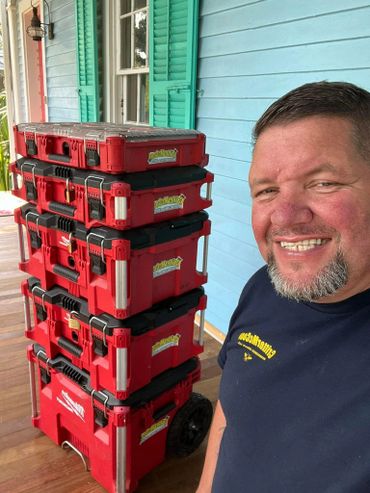 Smiling man next to a stack of red toolboxes on a porch.