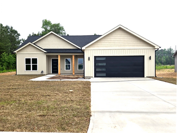 Modern beige house with black garage door and a spacious driveway.