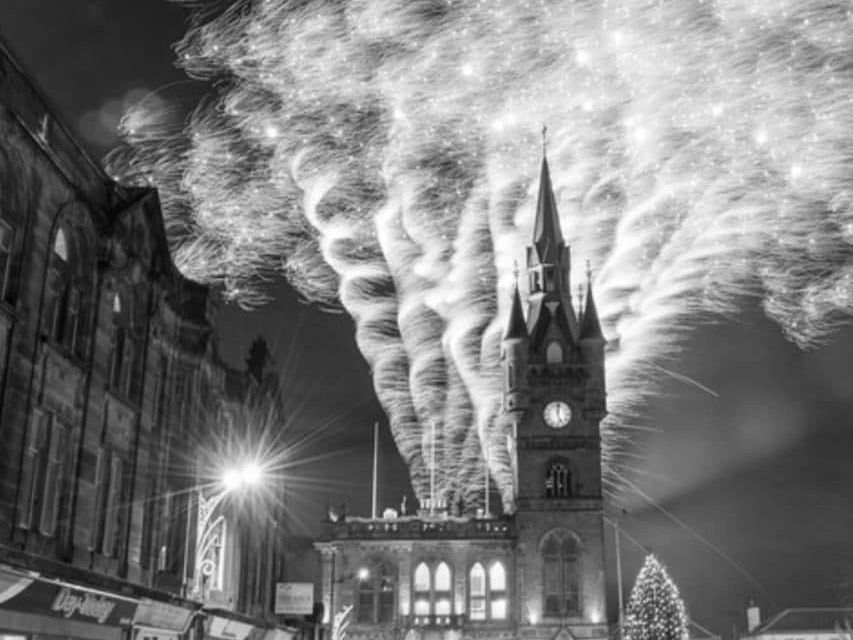 Fireworks explode above a clock tower in a festive nighttime scene.