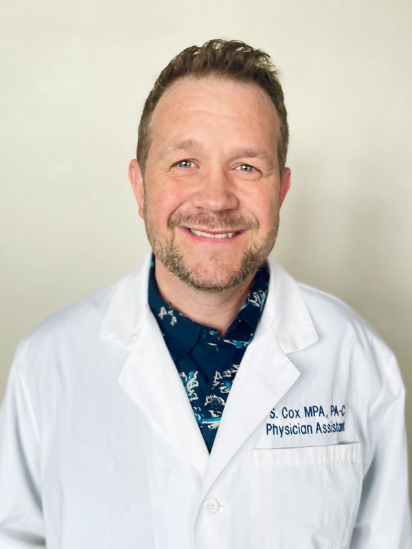Smiling male physician assistant in a white coat against a plain background.