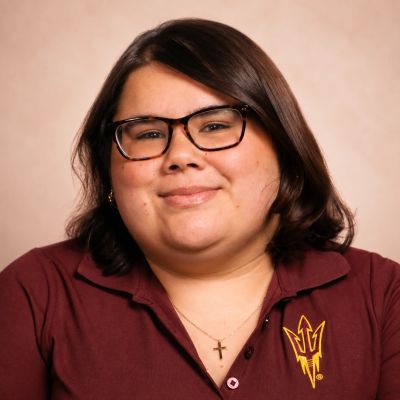 Smiling woman wearing glasses and maroon shirt with school logo.