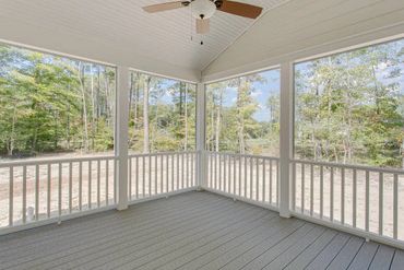 Spacious screened porch with ceiling fan overlooking a wooded area.