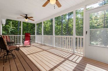 A bright screened porch with ceiling fans and seating overlooking greenery.