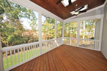 Spacious screened porch with wooden floor and ceiling fans overlooking trees.