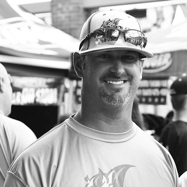 Smiling man wearing a baseball cap and reflective sunglasses.