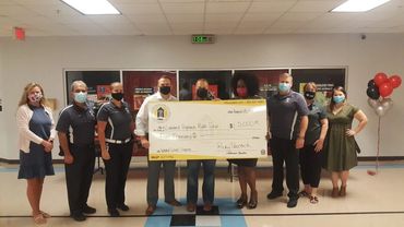 Group holding a large donation check in a school hallway.