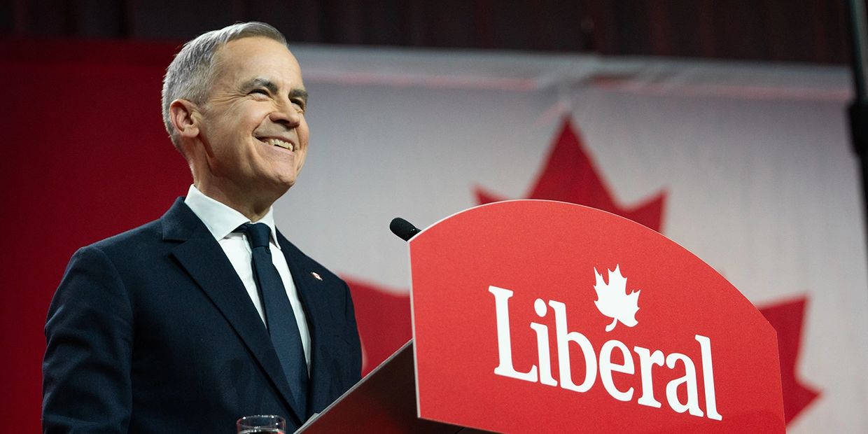 Smiling politician speaking at Liberal Party event with Canadian flag backdrop.