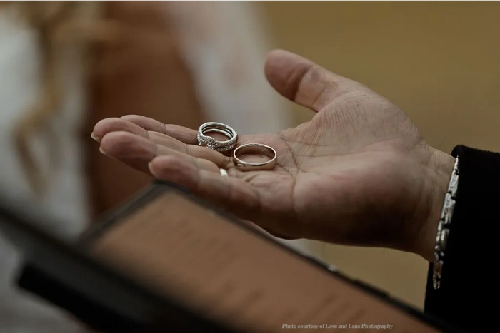 Closeup on an officiant's hand holds 2 rings above a script.