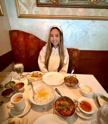 Woman smiling and sitting at a table with Indian food laid out in front of her.