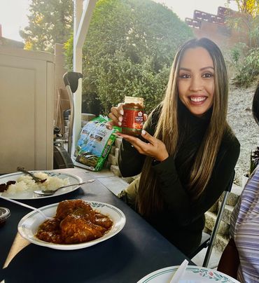 Woman smiling and sitting down at a table outside eating Filipino food.