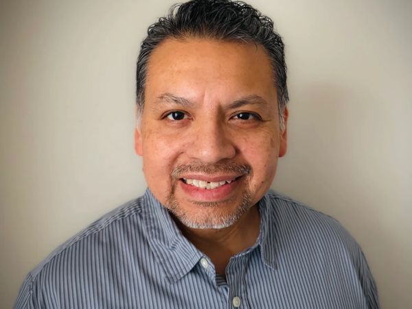 Smiling man with short hair and a striped shirt against a plain background.