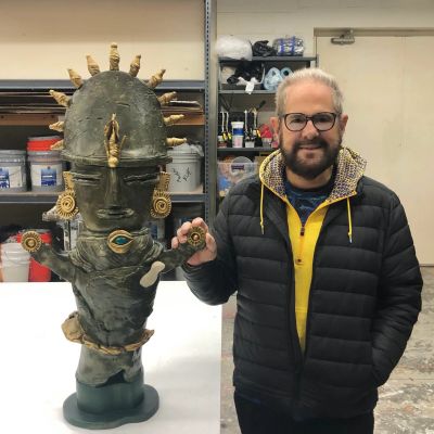 Man posing with a large tribal-style sculpture.