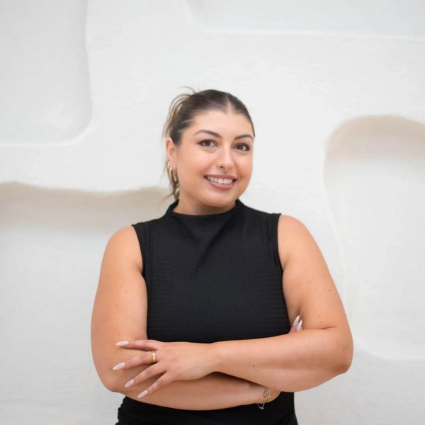 Confident woman in black sleeveless top smiling with arms crossed.