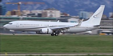A white commercial airplane landing on a runway with buildings and mountains in the background.
