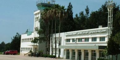 Exterior view of Qamishli Airport with control tower and palm trees.