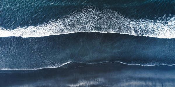 Aerial view of ocean waves crashing on a dark sandy beach.