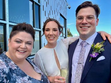 Three people smiling in formal attire at an outdoor event.