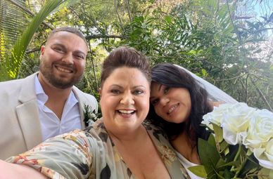 Group selfie of three smiling people outdoors at a wedding.