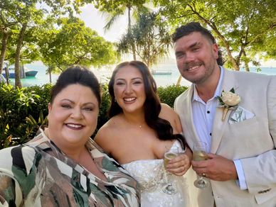 Three people smiling at a wedding outdoors.