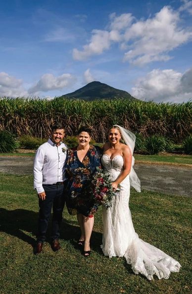 Newlyweds with a guest posing outdoors on their wedding day.