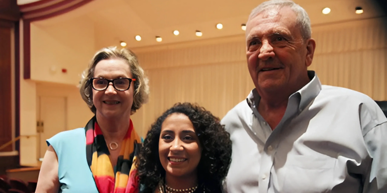 Three people smiling together inside a well-lit auditorium.