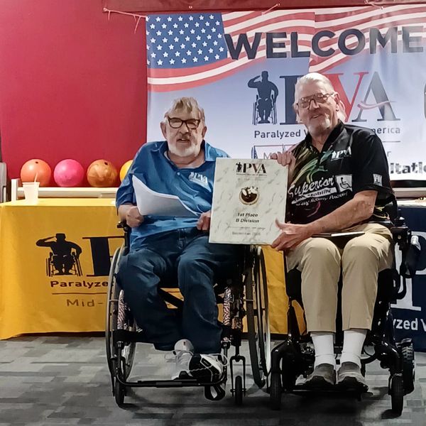 Two men in wheelchairs holding a PVA award certificate.