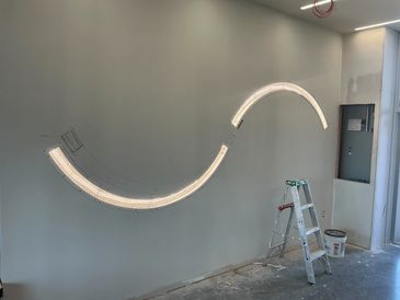 Light installation in progress on a wall with a ladder and paint bucket nearby.