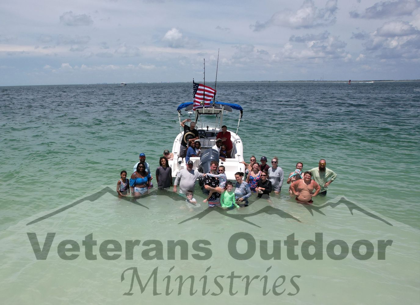 Group of people standing in shallow ocean water near a boat with an American flag.
