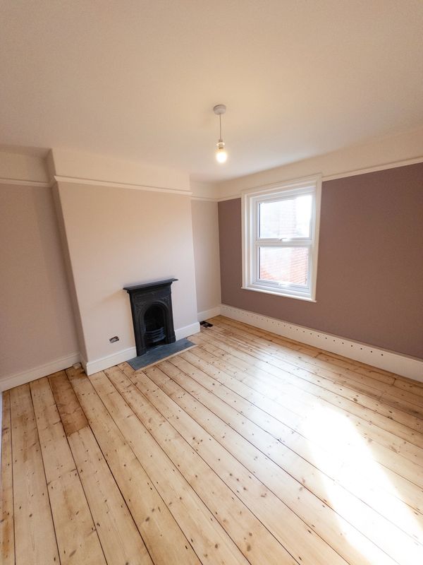 Empty room with wooden floor, small fireplace, and a window letting in natural light.