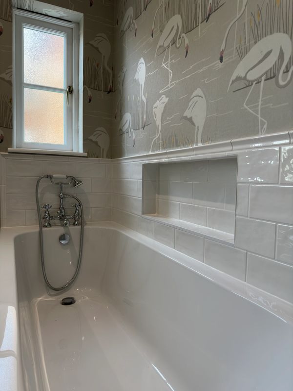 White bathtub with chrome fixtures and flamingo wallpaper near frosted window.