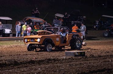Vintage off-road vehicle racing on a dirt track at night with spectators watching.