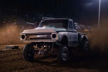 A lifted vintage Chevrolet truck kicking up dirt at night.